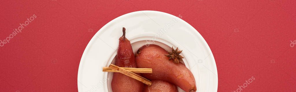 top view of delicious pear in wine with cinnamon and anise on plate on red background, panoramic shot
