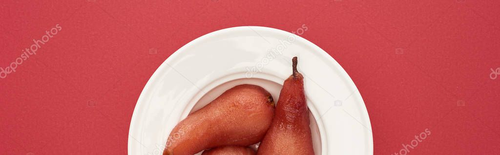 top view of delicious pears in wine on plate on red background, panoramic shot