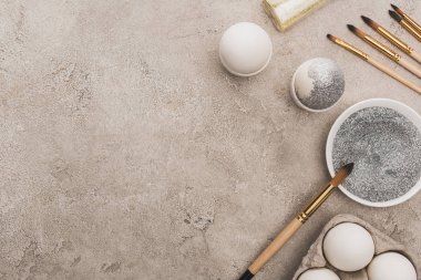 Tavuklu yumurta, gümüş ve altın parıltılı gri beton yüzeyde boya fırçaları.