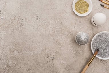 Tavuklu yumurta, gümüş ve altın parıltılı gri beton yüzeyde boya fırçaları.
