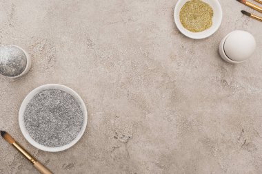 Tavuklu yumurta, gümüş ve altın parıltılı gri beton yüzeyde boya fırçaları.