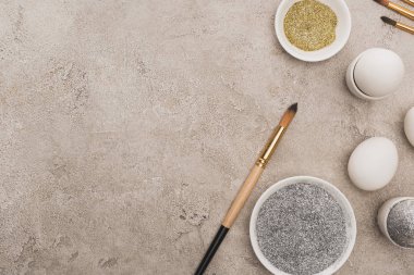 Tavuklu yumurta, gümüş ve altın parıltılı gri beton yüzeyde boya fırçaları.