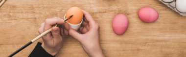 cropped view of woman coloring Easter eggs with paintbrush at wooden table, panoramic shot clipart