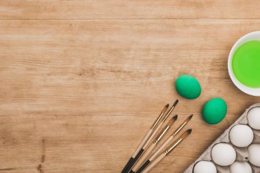 Tavuklu yumurta ve ahşap masadaki boya fırçalarının yanındaki kasede yeşil suluboya boya.