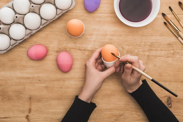 Καλλιεργημένη Άποψη Της Γυναίκας Χρωματισμός Πασχαλινά Αυγά Πινέλο Ξύλινο Τραπέζι — Φωτογραφία Αρχείου