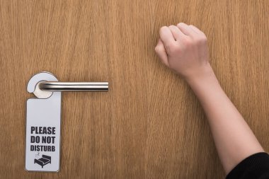 cropped view of woman knocking at door with please do no disturb sign  clipart