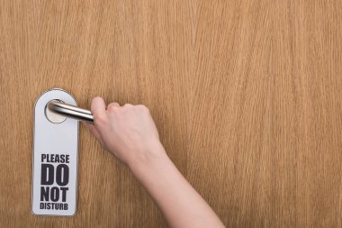 cropped view of woman holding door handle with please do no disturb sign  clipart