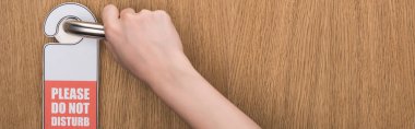 partial view of woman holding door handle with please do no disturb sign, panoramic shot clipart