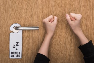 cropped view of woman knocking at door with do no disturb sign  clipart