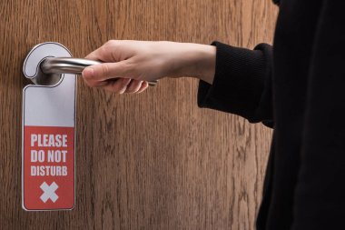 partial view of woman holding door handle with please do no disturb sign  clipart