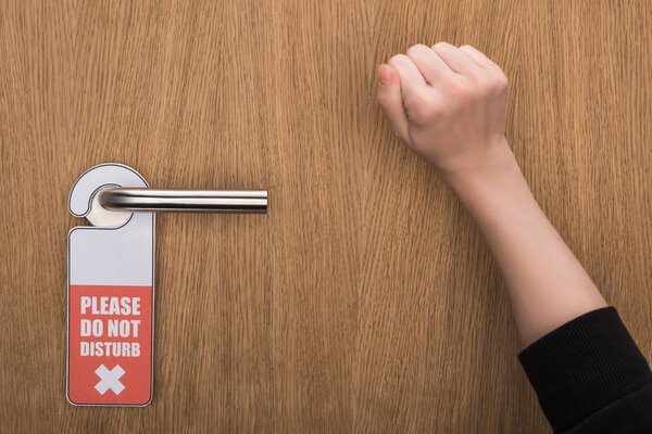 cropped view of woman knocking at door with please do no disturb sign 