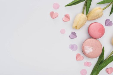 Beyaz lalelerin üst görüntüsü, pembe badem kurabiyeleri ve mor kalpler.