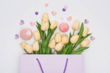 Lalelerin üst görüntüsü, pembe badem kurabiyeleri ve mor kalpler beyaz torbada izole edilmiş.