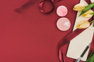 İpek kurdeleli lalelerin üst görünümü, Makaronlar ve kırmızı üzerine izole edilmiş kalemle boş defter
