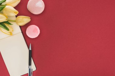 Lalelerin üst görüntüsü, pembe badem kurabiyeleri ve kırmızı kalemle izole edilmiş boş bir defter.
