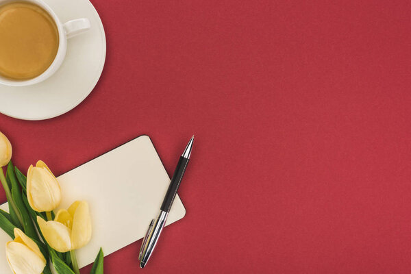 top view of tulips and empty notebook with pen near cup of coffee isolated on red