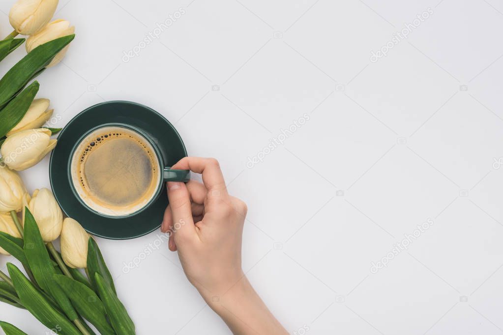 cropped view of woman holding cup of fresh coffee near tulips isolated on white