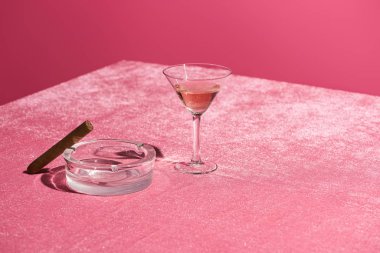 Kül tablasında puronun yanında pembe şarap. Pembe, kızsı bir konseptte izole edilmiş kadife kumaş.