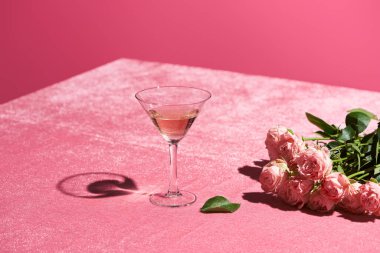 Gül şarabı, kadife gül buketinin yanında pembe kumaş üzerinde pembe, kızsı bir konseptte izole edilmiş.