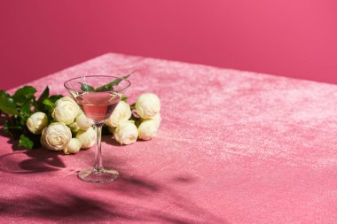 Gül şarabı, kadife gül buketinin yanında pembe kumaş üzerinde pembe, kızsı bir konseptte izole edilmiş.