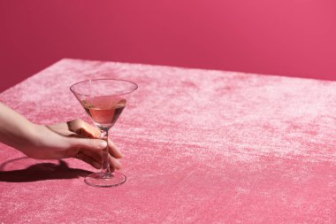 Kırpılmış bir kadın, kadife kumaş üzerinde gül şarabı bardağını tutuyor pembe, kızsı bir konseptte izole edilmiş. 