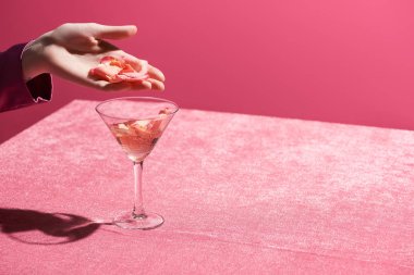 Kırpılmış bir kadın, kadife kumaşın üzerinde cama taç yaprakları yapıştırıyor pembe, kızsı bir konseptte izole edilmiş. 