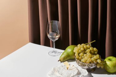Klasik Camembert peyniri, beyaz şarap ve bej rengi perdenin yakınındaki masada meyvelerle yaşam.