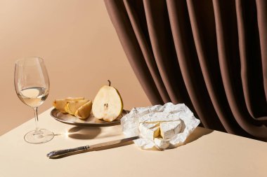 Klasik hayat, armut, beyaz şarap ve bej üzerine izole edilmiş perdenin yanındaki masada Camembert peyniri