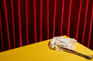 classic still life with Camembert near knife on yellow table near red curtain clipart