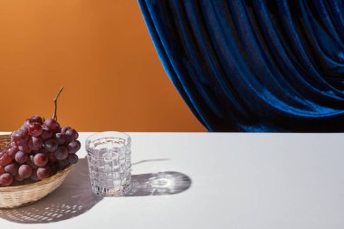 Klasik natürmortlu yaşam, beyaz masanın üzerindeki cam kadife perdenin yanındaki portakalda izole edilmiş.