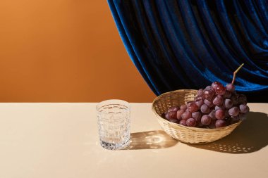 Klasik hayat üzümlü, bej masadaki cam kadife perdenin yanında turuncu üzerinde izole edilmiş.