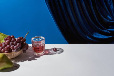 Klasik hayat üzümlü, bardaklı içki beyaz masada kadife perdenin yanında mavi izole edilmiş.