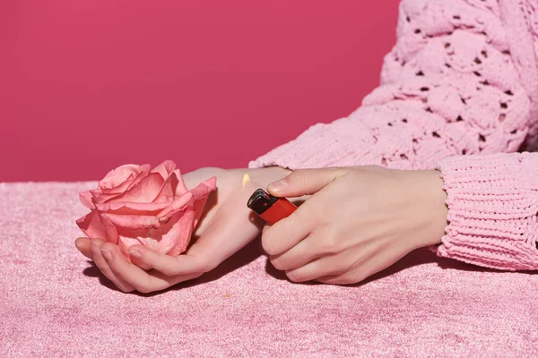 ピンク色のガーリッシュなコンセプトで孤立したベロアクロスにバラとライターを持つ女性のクロップドビュー — ストック写真