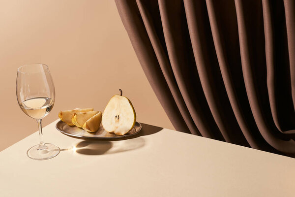 classic still life with pear and white wine on table near curtain isolated on beige