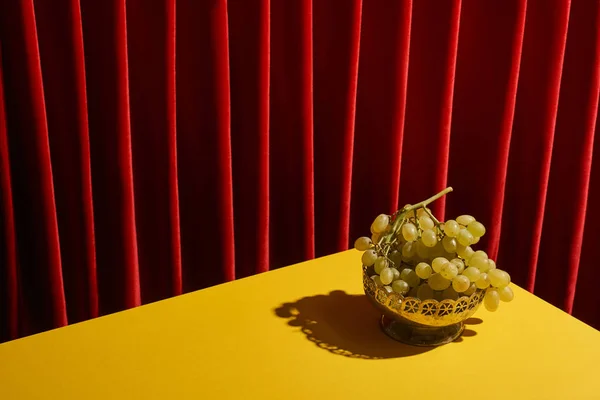 赤いカーテンの近くの黄色のテーブルの上に緑のブドウと古典的な静物画 — ストック写真