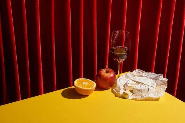 赤のカーテンの近くの黄色のテーブルの上に赤ワインと果物のガラスの近くにCamembertと古典的な静物画 — ストック写真