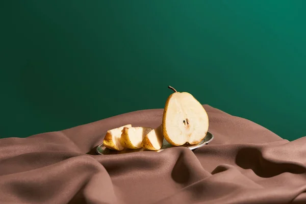 classic still life with cut pear on silver plate on table with brown tablecloth isolated on green