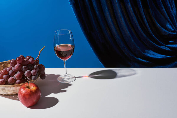 classic still life with fruits, red wine on white table near velour curtain isolated on blue
