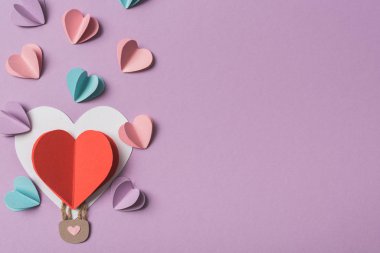 Kalbin etrafındaki renkli kağıt kalplerin üst görüntüsü menekşe arkaplanda kağıt balon şeklinde.