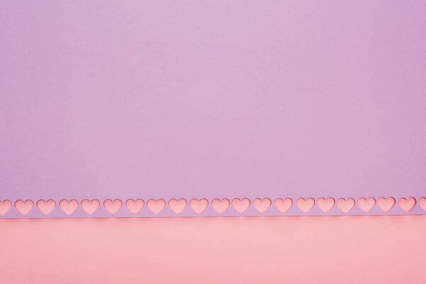 верхний вид фиолетовой бумаги с вырезанными сердцами на розовом фоне

