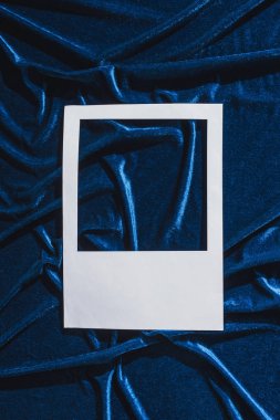 Mavi kadife kumaş üzerinde boş beyaz fotoğraf çerçevesi üst görünümü