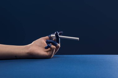 Kırpılmış kadın eli, mavi üzerine izole edilmiş sigara tutan boyalı parmaklar.