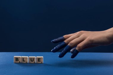 Kırpılmış kadın eli görüntüsü, mavi harflerle izole edilmiş küplerin yanında boyanmış parmaklar.