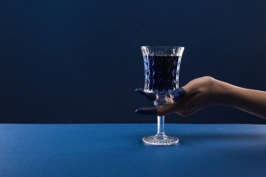 Kırpılmış kadın eli, boyalı parmaklarıyla elinde cam, mavi bardakta izole edilmiş içki.