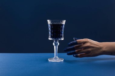 Kırpılmış kadın eli görüntüsü, boyalı parmaklar, cam kırıkları ve mavi üzerine izole edilmiş içki.