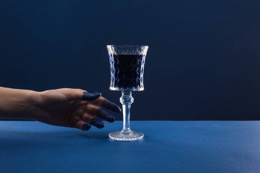 Kırpılmış kadın eli görüntüsü, boyalı parmaklar, cam kırıkları ve mavi üzerine izole edilmiş içki.