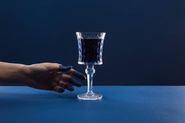 cropped view of female hand with painted fingers near faceted glass with drink isolated on blue clipart