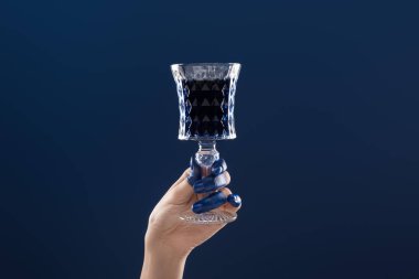 Kırpılmış kadın eli, boyalı parmaklarıyla elinde cam, mavi bardakta izole edilmiş içki.