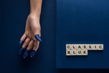 Kırpılmış mavi arka planda küplere yazılmış klasik mavi harflerin yanında boyalı parmakları olan kadın manzarası