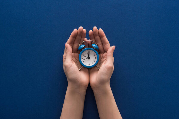 cropped view of woman holding alarm clock on blue background